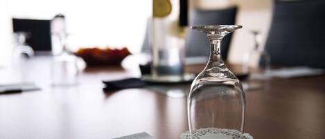 A clear glass decanter on a table with a lace doily, a notebook, and a blurred background with a lamp and a vase.