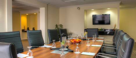 A conference room with a long table, black leather chairs, and a flat-screen TV on the wall.