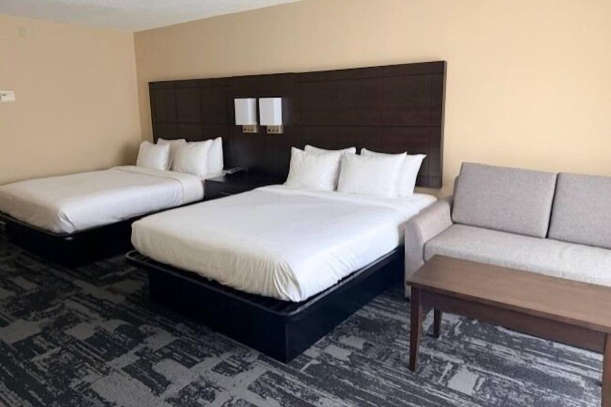 A hotel room with two single beds and a double bed, a sofa, and a small table.