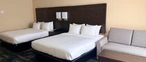 A hotel room with two single beds and a double bed, a sofa, and a small table.