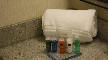 A bathroom counter with toiletries including a white towel, a bottle of lotion, and several other personal care products.