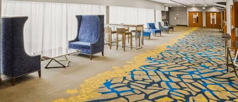 A hotel lobby with a long carpeted corridor, seating area with chairs, and a reception desk.