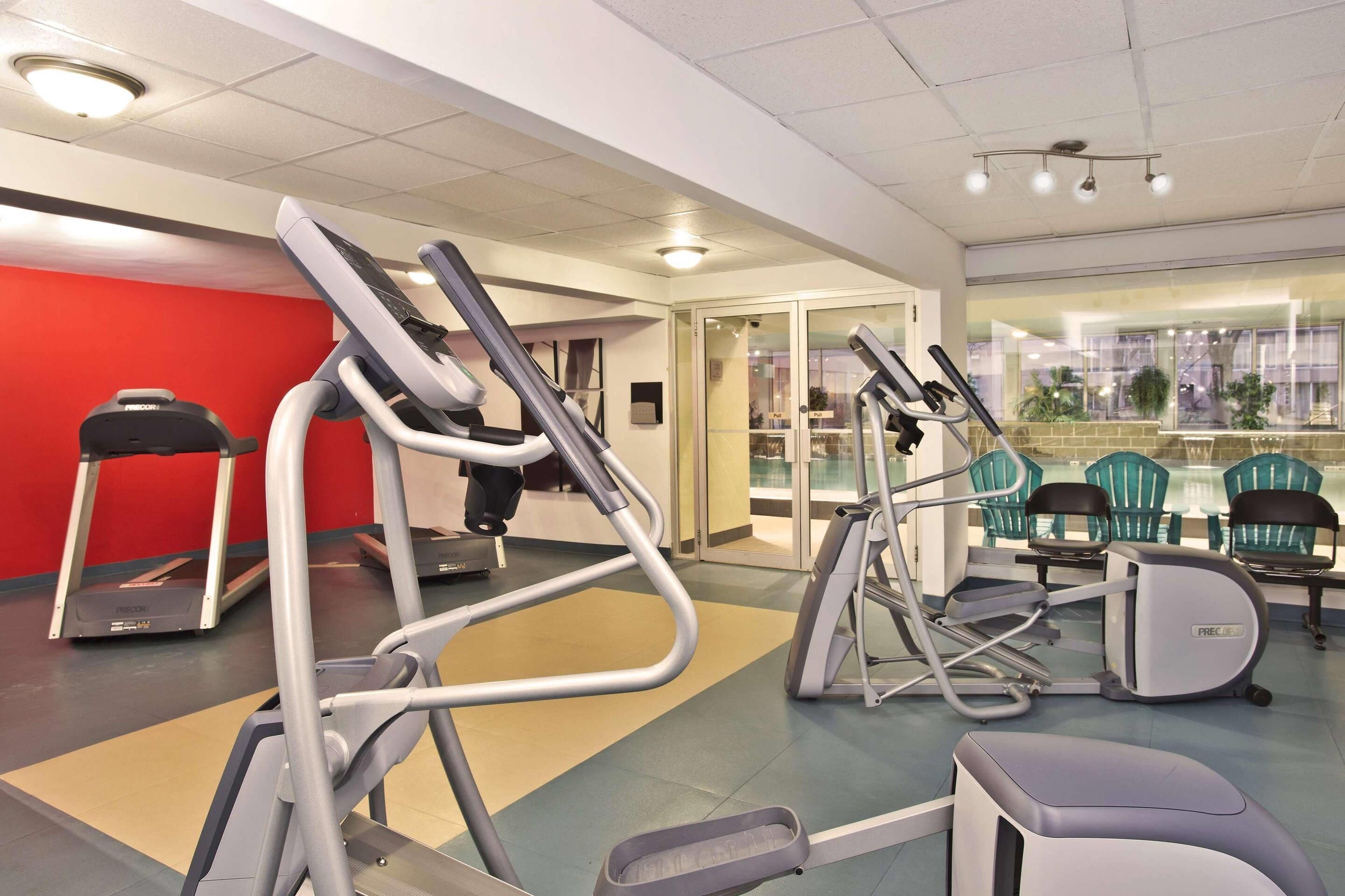 Un gimnasio con cintas de correr, elípticas y un espejo grande.