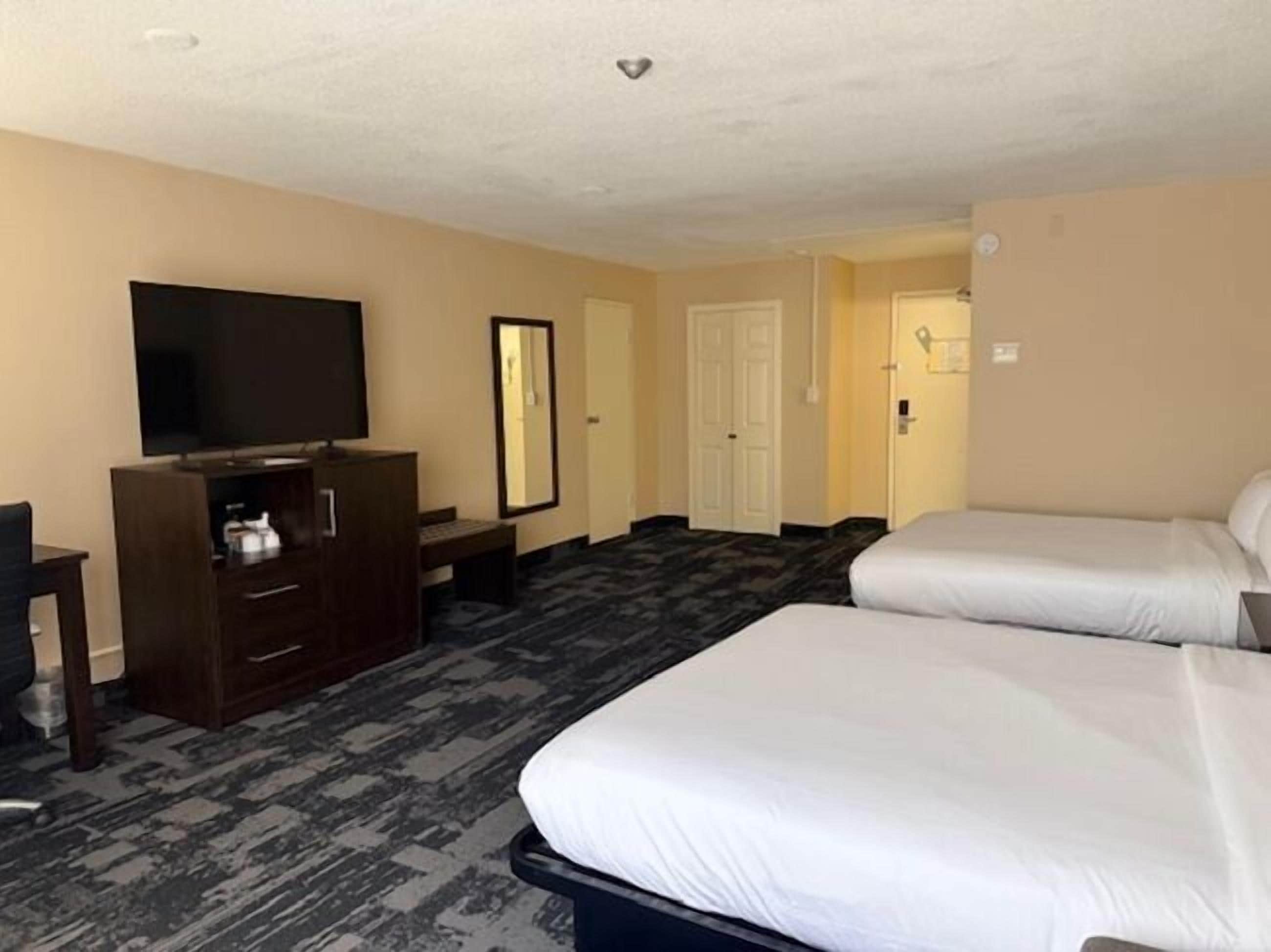 A hotel room with two beds, a TV, a desk, and a mirror.