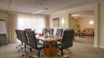 A conference room with a large table, six chairs, a whiteboard, and a sofa in the background.