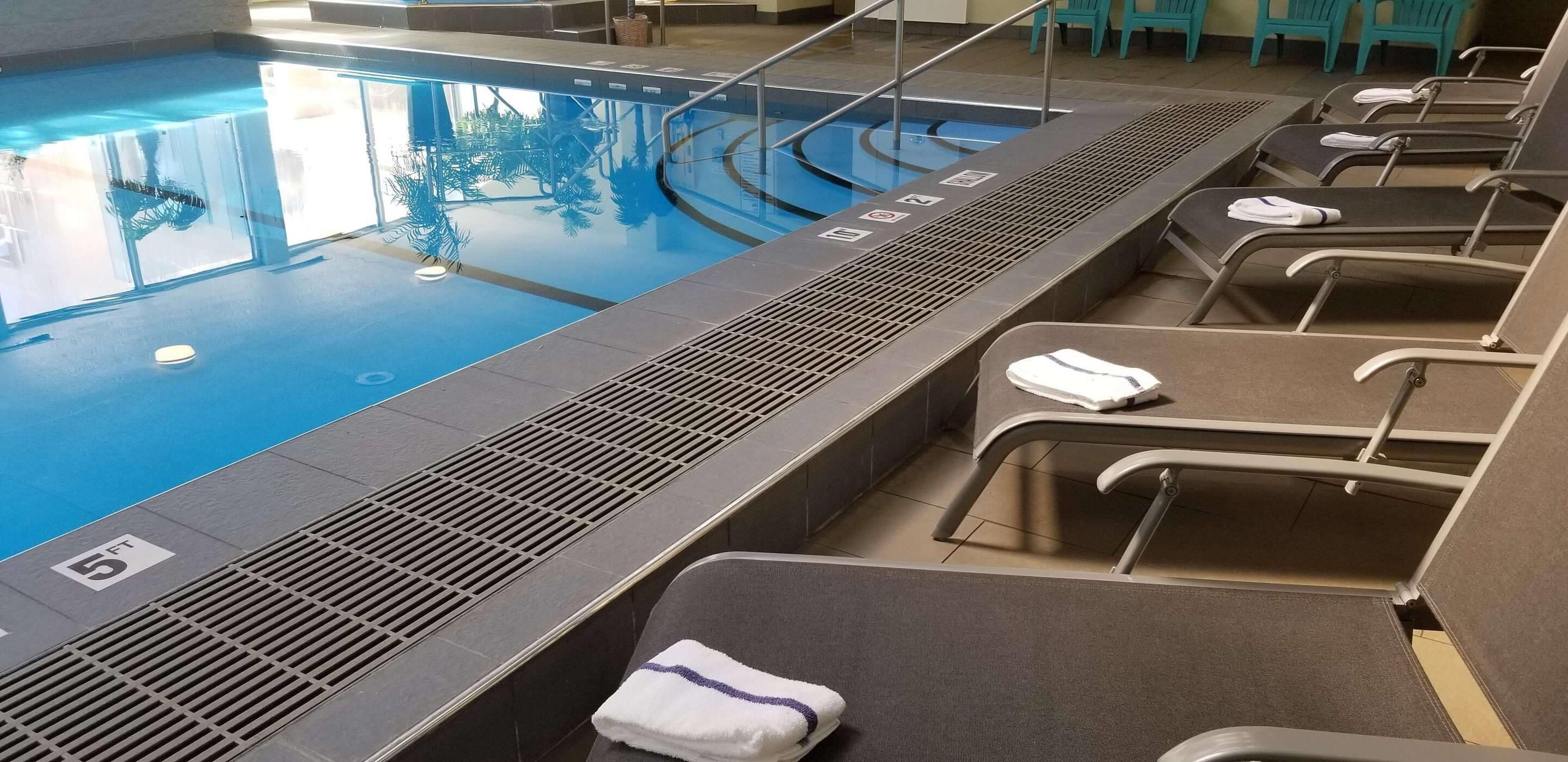 A swimming pool with a diving board, lounge chairs with towels, and a tiled floor.