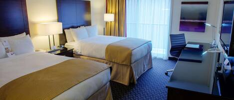 Una habitación de hotel con dos camas, un escritorio con una silla, un televisor y una ventana con cortinas.