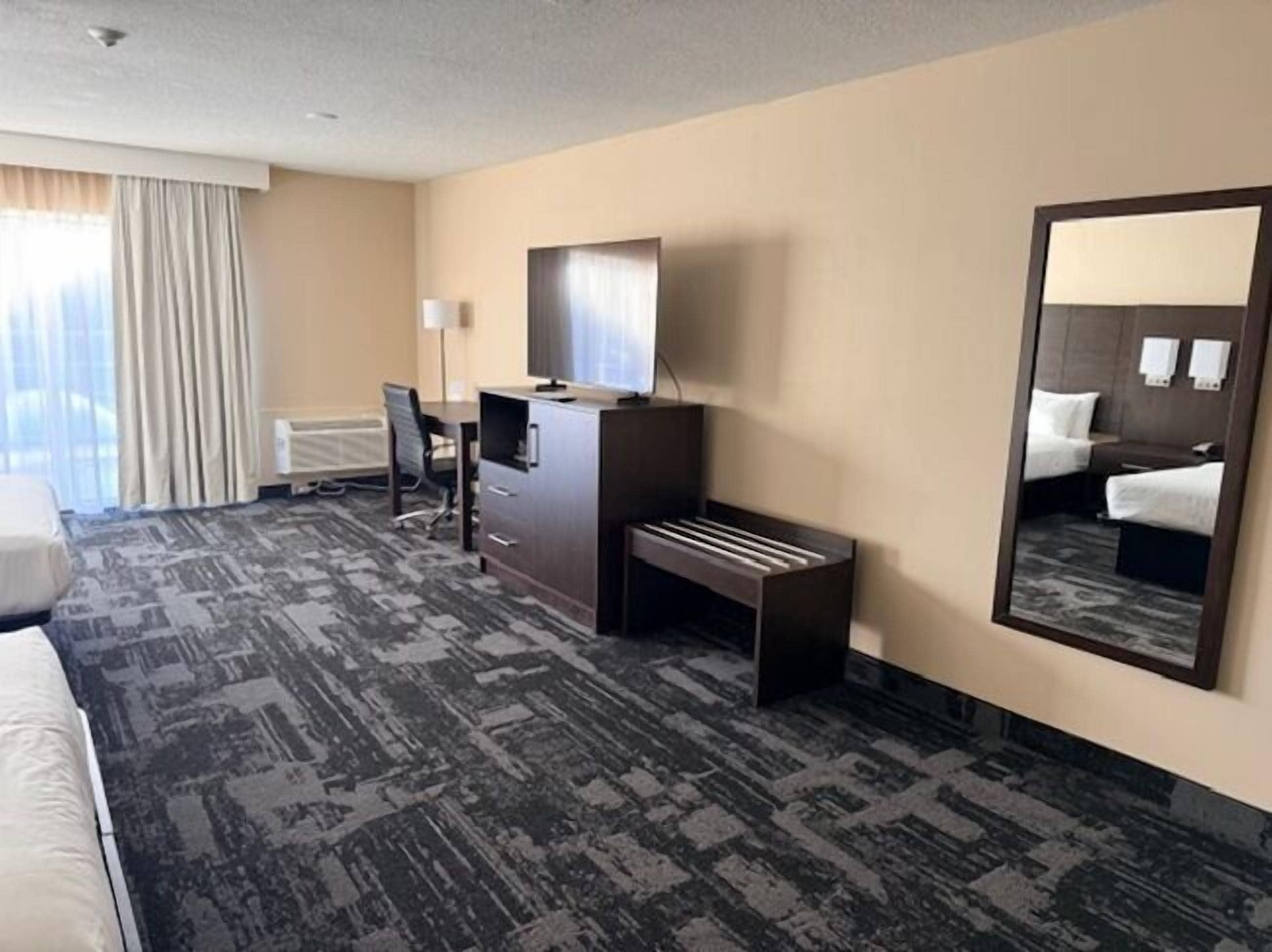 A hotel room with a large bed, a desk, a chair, a dresser, and a mirror.