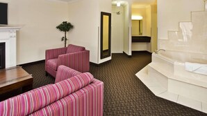 A hotel room with a fireplace, striped sofa, a large mirror, a bathtub, and a carpeted floor. - Radisson Hotel Sudbury (Sudbury)