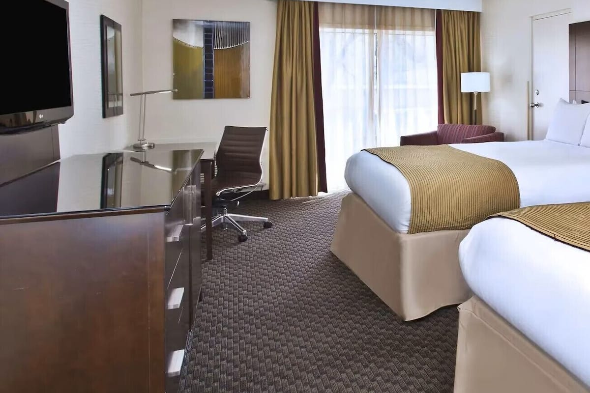 A hotel room with a bed, a desk, a chair, a TV, and a window with curtains.