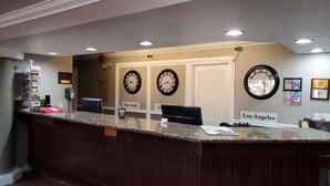 A reception desk with clocks labeled "New York" and "Los Angeles," a check-out counter, and a bulletin board with various notices. - Ramada by Wyndham Barstow (Barstow)