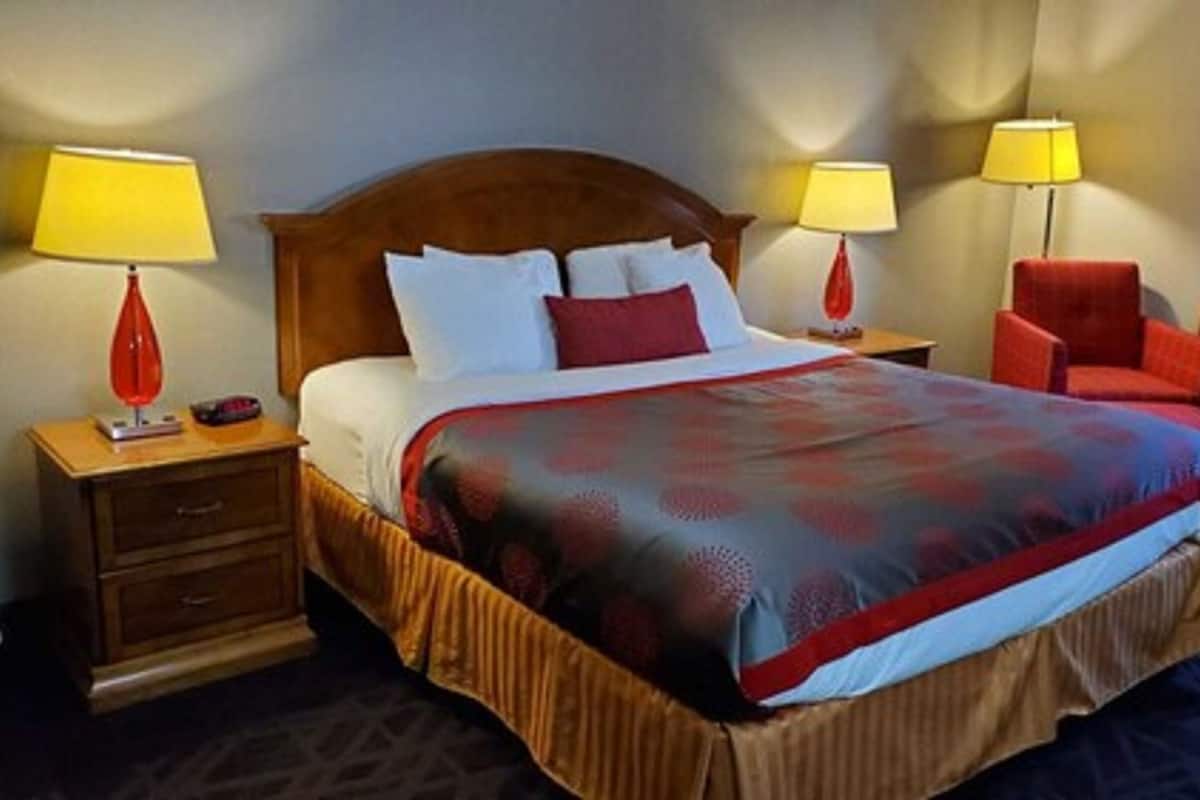 A hotel room with a large bed, two bedside tables, a red armchair, and two lamps.
