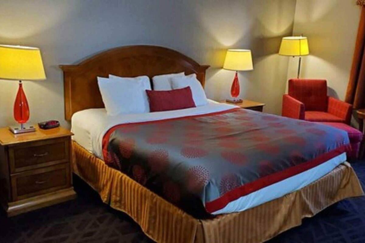 A hotel room with a large bed, two bedside tables, a chair, and two lamps.