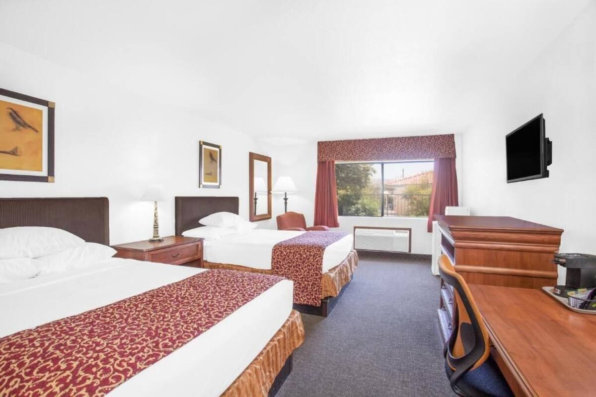A hotel room with two beds, a desk, a chair, a TV, and a window with a view.