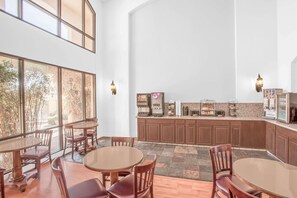 A spacious dining area with high ceilings, large windows, and a kitchen with various appliances.