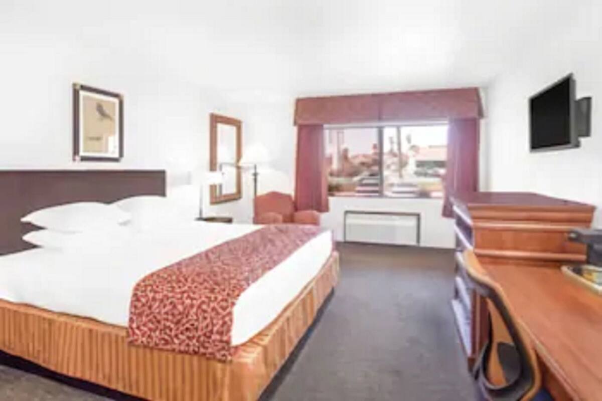 A hotel room with a bed, a desk, a chair, a window, and a picture on the wall.