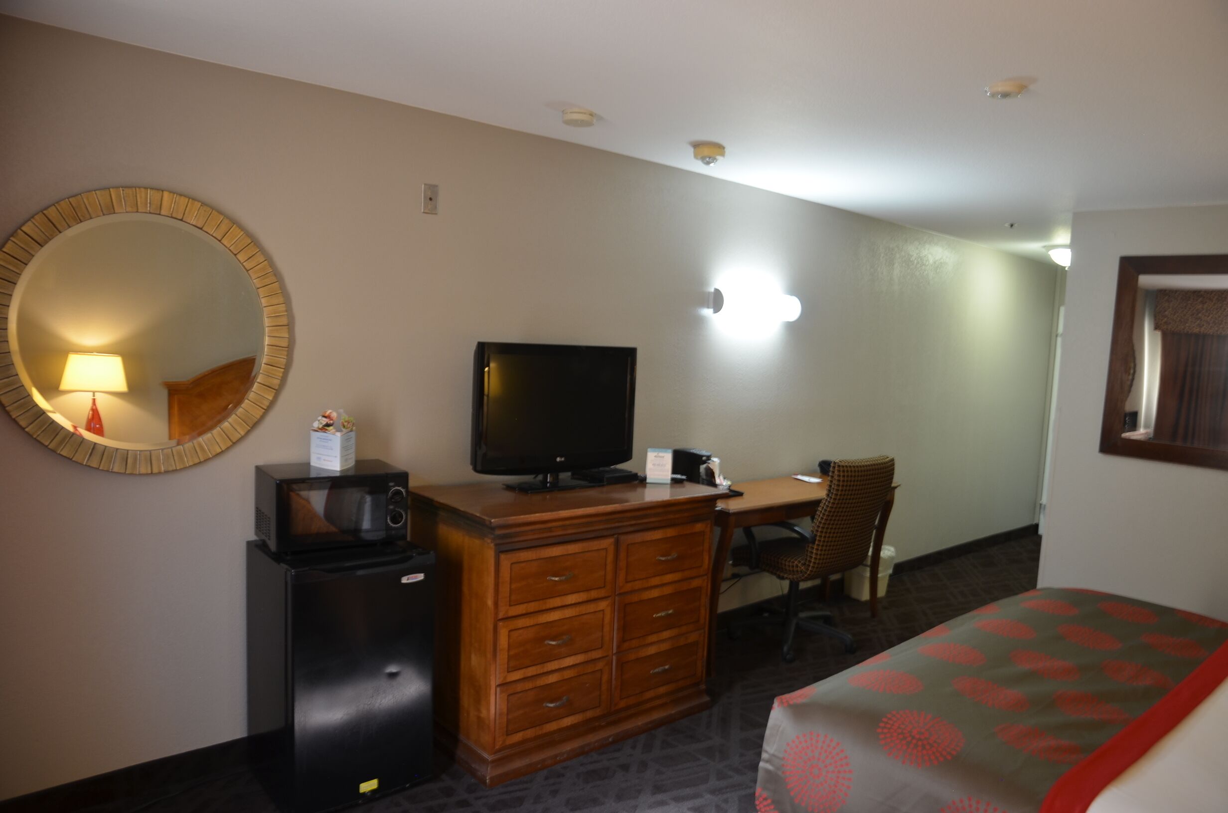 Une chambre d’hôtel avec un bureau en bois, une télévision, un four à micro-ondes, une commode et un lit recouvert d’une couvre-lit à motifs.
