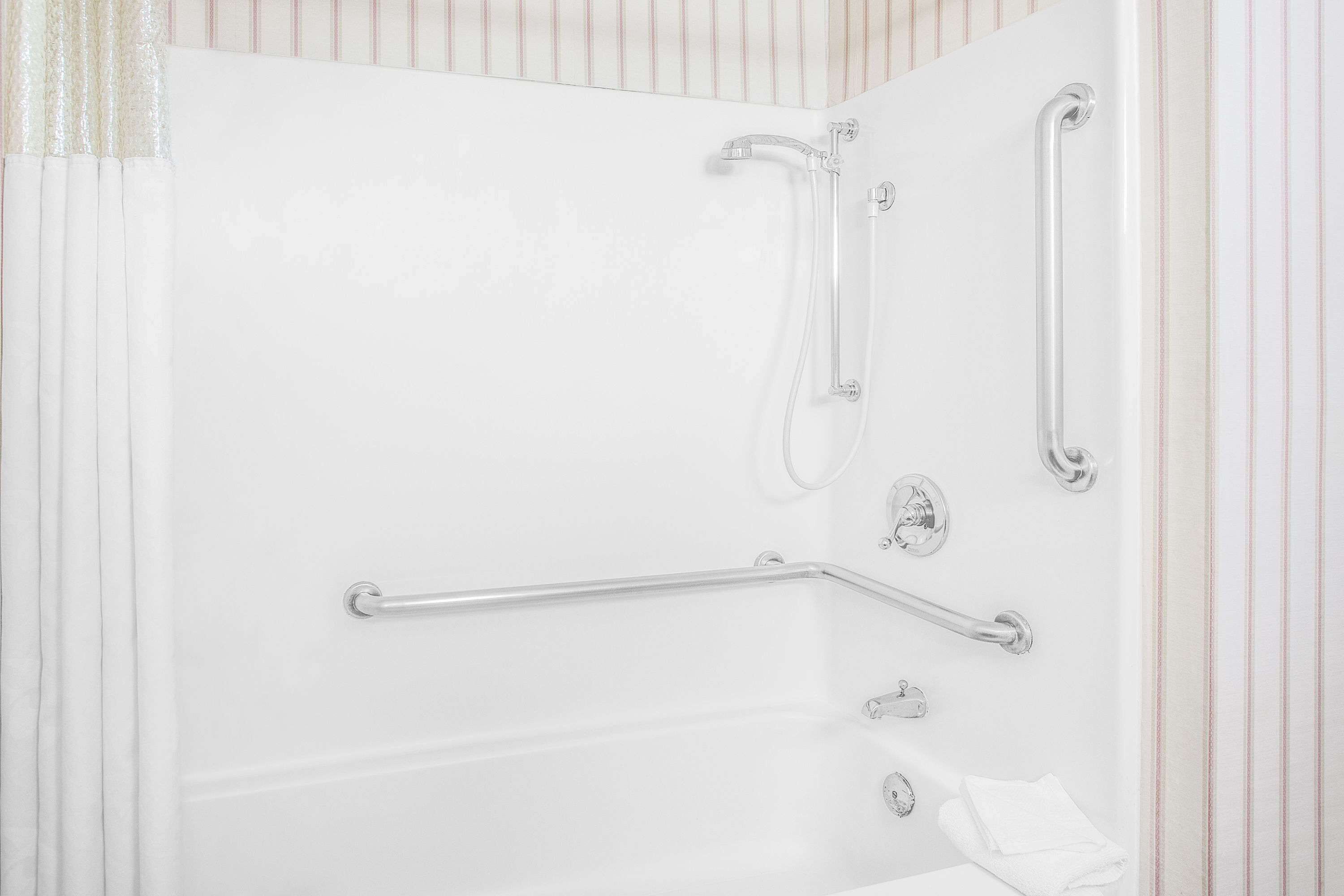 A white bathtub with grab bars and a showerhead.