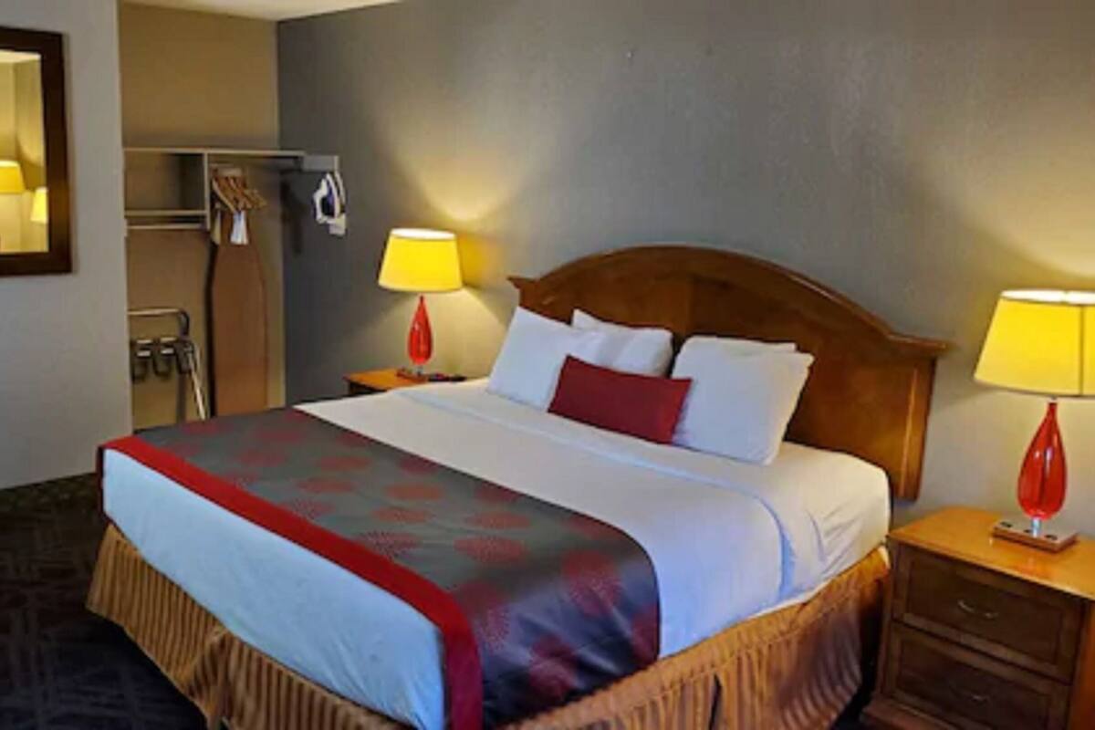 A hotel room with a large bed, two bedside lamps, a wooden headboard, a mirror, and a wardrobe.