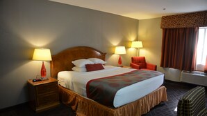 A hotel room with a large bed, two bedside tables, a chair, and a window with curtains. - Ramada by Wyndham Barstow (Barstow)