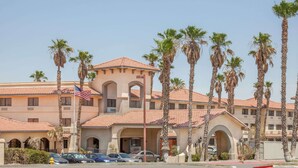 A hotel with a Mediterranean architectural style, featuring a central courtyard with palm trees and a red-tiled roof. - Ramada by Wyndham Barstow (Barstow)