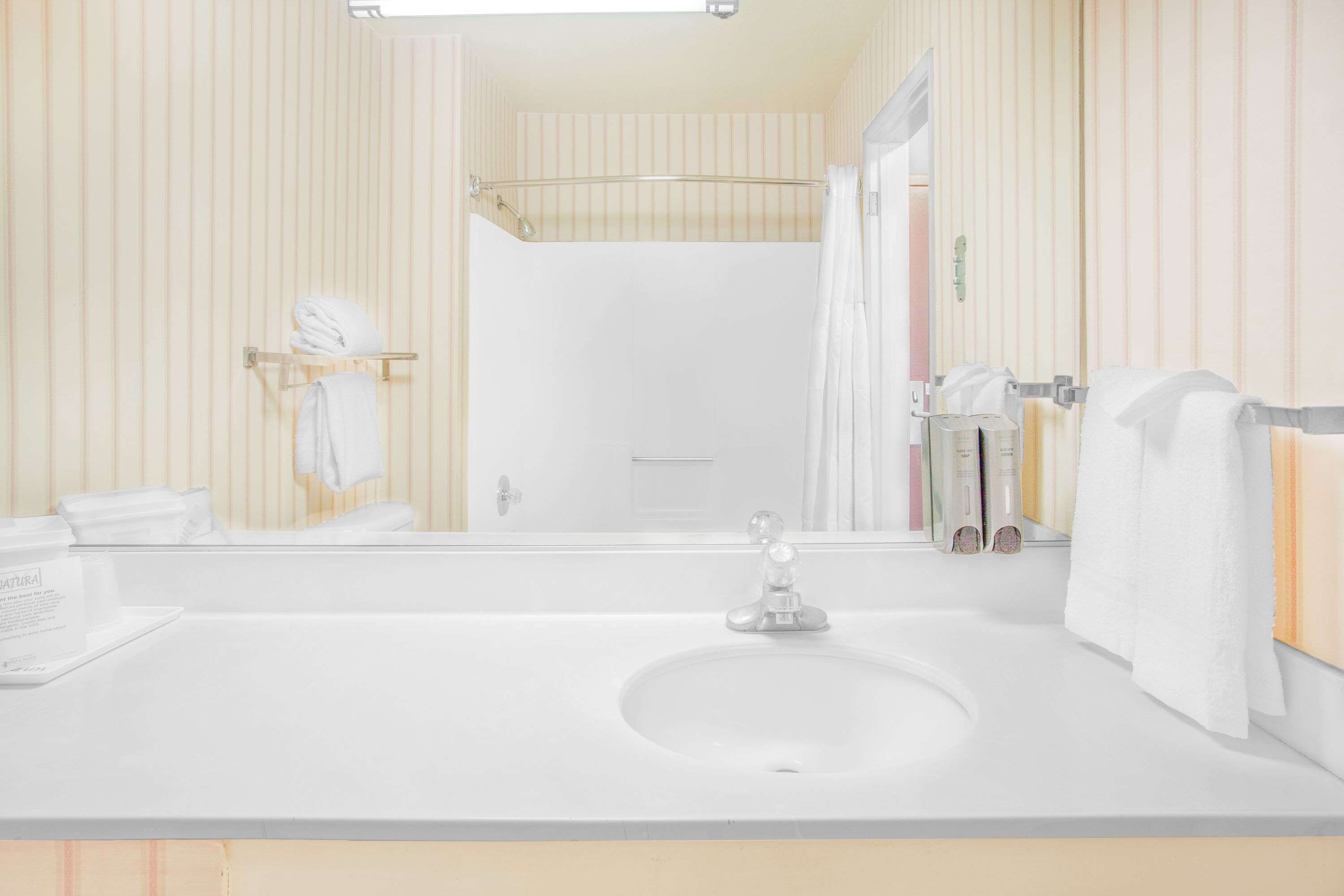 A bathroom with a white sink, a glass shower enclosure, and striped wallpaper.