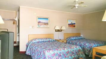 A hotel room with two beds, a desk, a chair, a television, and a ceiling fan.