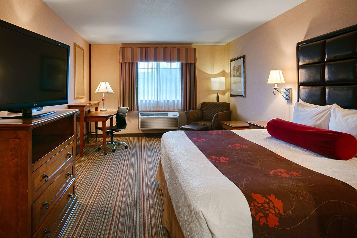 A hotel room with a bed, a desk with a chair, a television, a lamp, and a window with curtains.