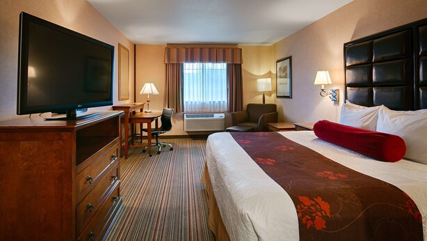 A hotel room with a bed, a desk with a chair, a television, a lamp, and a window with curtains.