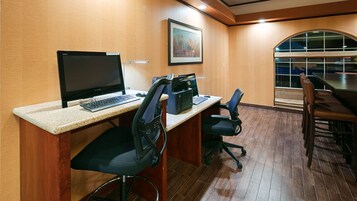 Un salón de conferencias con una computadora de escritorio, dos sillas de oficina, una impresora y un ventanal grande.