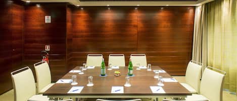 A conference room with a wooden table, white chairs, and glassware.
