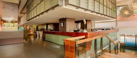 A modern hotel lobby with a reception desk, a staircase, and a view of the outdoors.