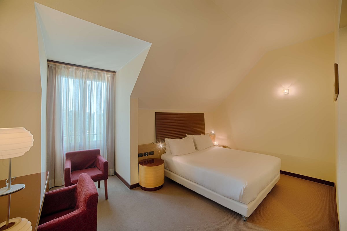 A hotel room with a bed, a chair, a lamp, and a nightstand.