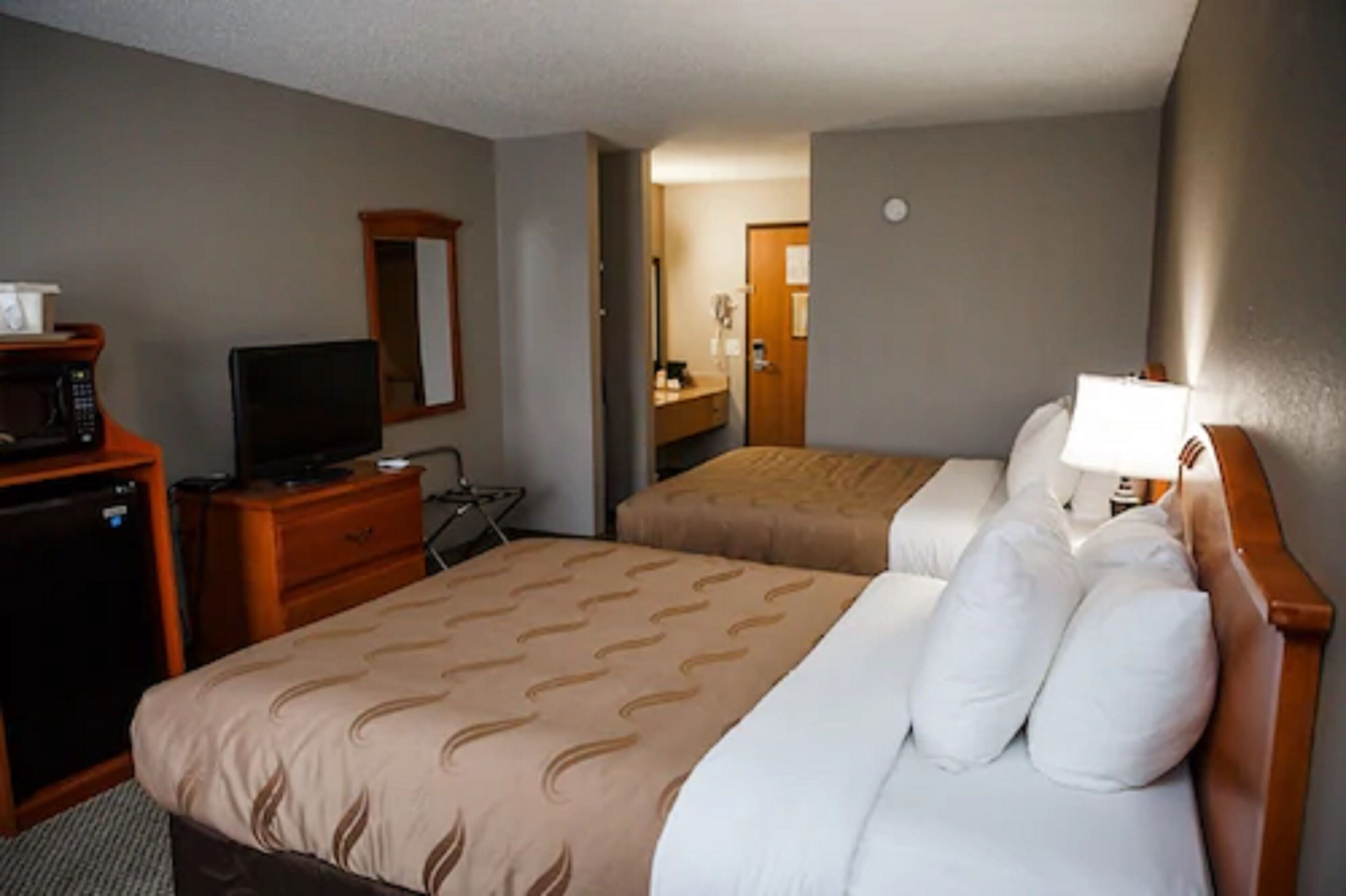 Habitación de hotel con dos camas, un escritorio con computadora, un microondas y un espejo.