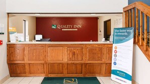 Un hall d’accueil d’hôtel avec un comptoir de réception en bois, un mur rouge sur lequel figure le nom de l’hôtel et un panneau indiquant les avantages offerts.