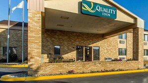 Un bâtiment de la chaîne Quality Inn avec une façade en briques, un ciel bleu dégagé et un drapeau américain.