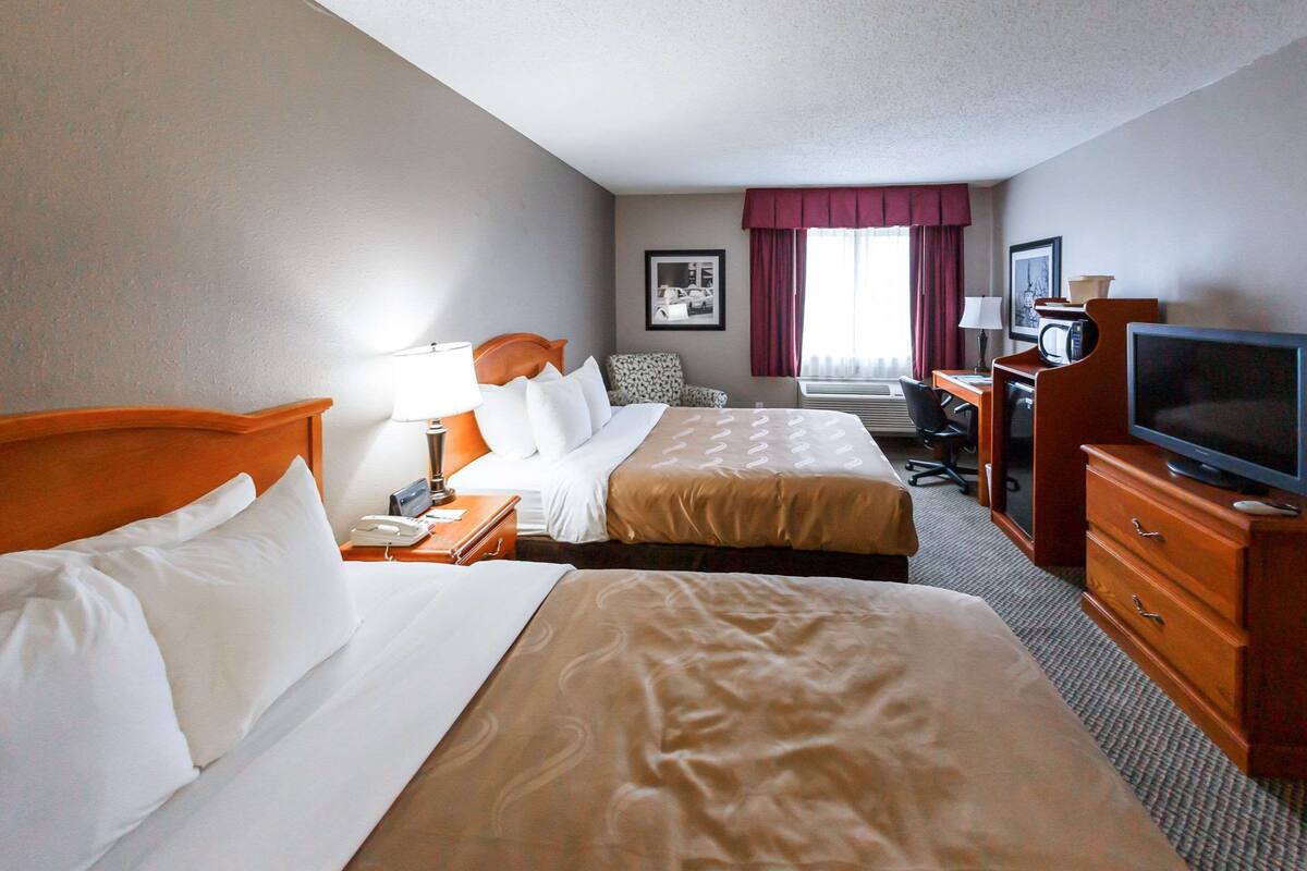 A hotel room with two beds, a desk, a television, and a chair.