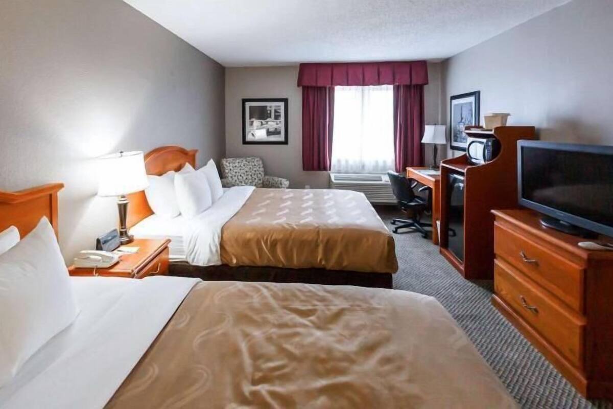 A hotel room with two beds, a desk, a television, and a chair.