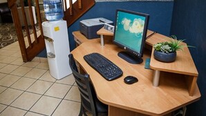 Un bureau en bois avec un ordinateur de bureau, un clavier et une souris. On y trouve également un distributeur d’eau, une imprimante et une petite plante en pot.