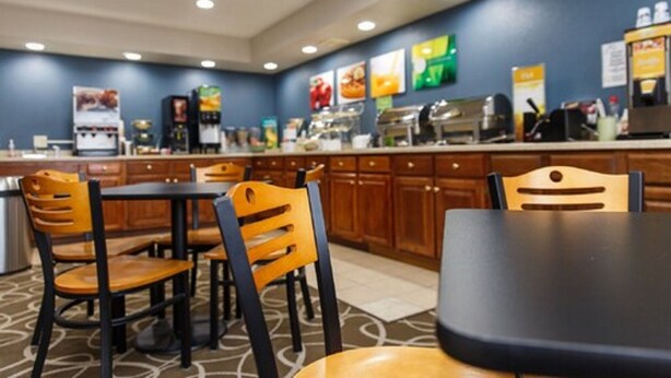Un espace repas d’hôtel avec des chaises et des tables en bois, une machine à café et un comptoir de buffet.
