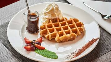 A plate with a waffle, whipped cream, and syrup, accompanied by strawberries and a mint leaf.
