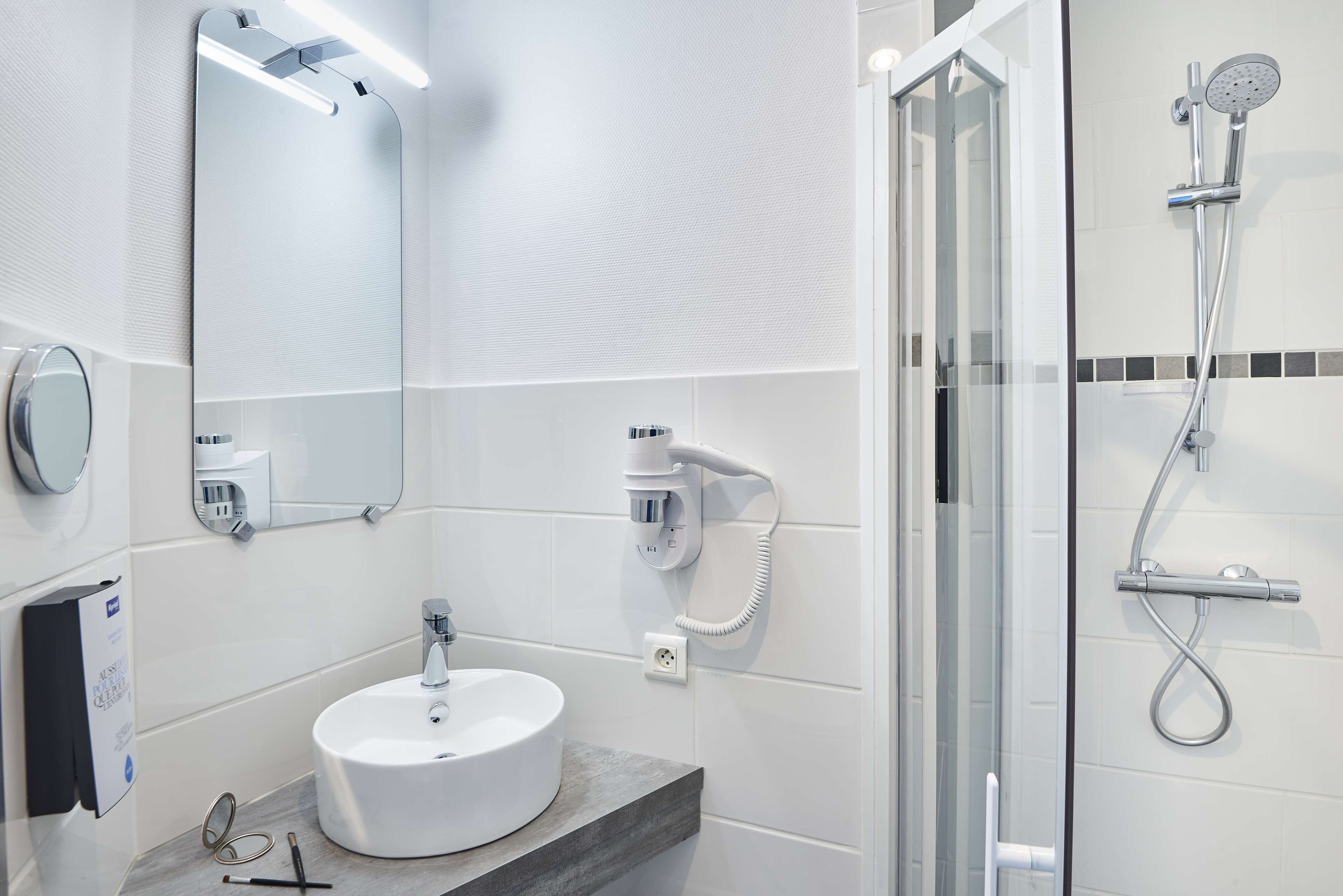 A modern bathroom with a white sink, a large mirror, a handheld showerhead, and a glass-enclosed shower.