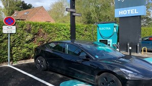 Un área de estacionamiento con estaciones de carga para vehículos eléctricos, un letrero de hotel y flechas direccionales en el pavimento.