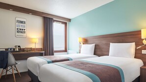 Habitación de hotel con dos camas, un escritorio con lámpara, una silla y una ventana con cortinas.
