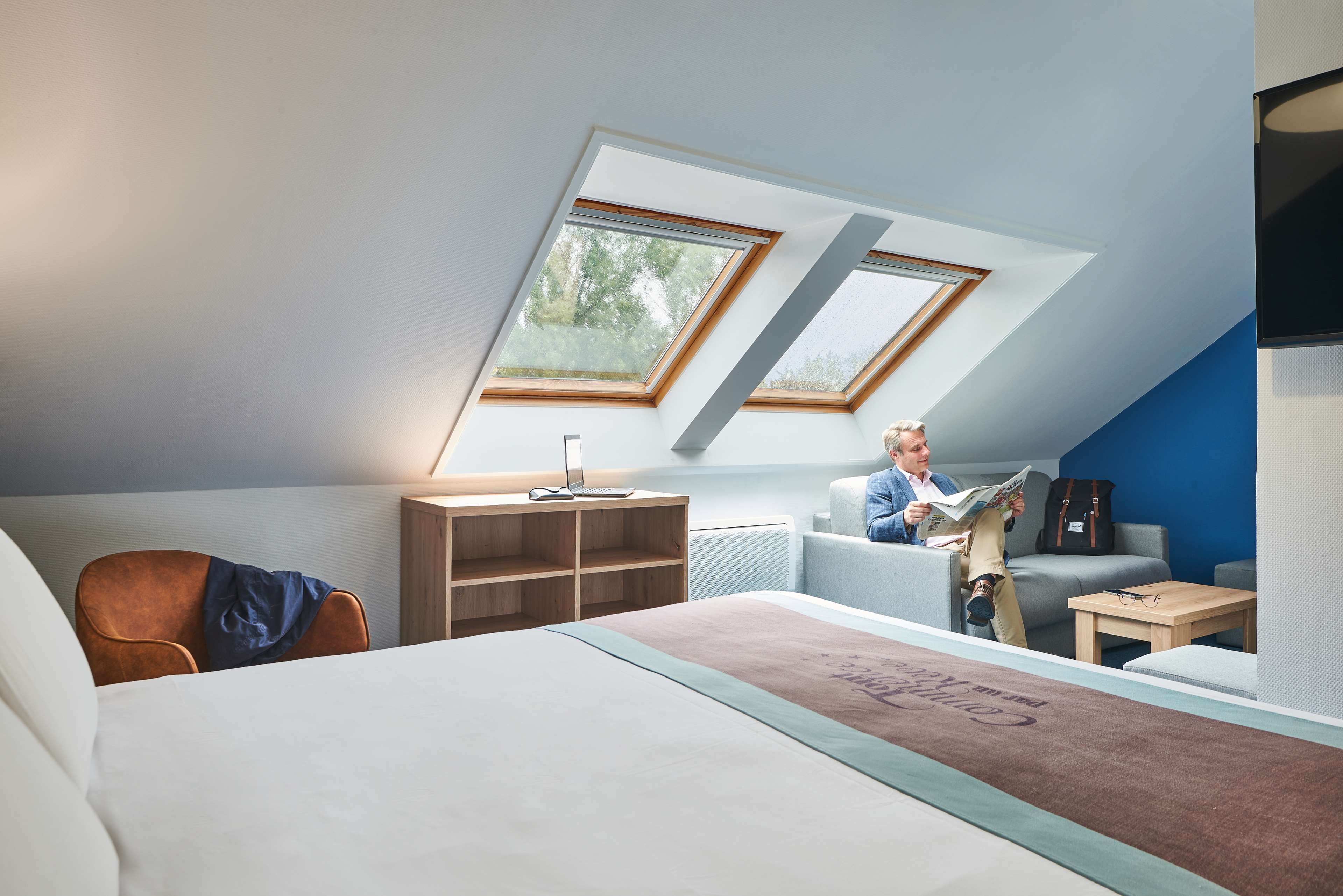 Une chambre de style loft moderne, dotée de fenêtres de toit, d’un lit, d’un bureau et d’un coin lecture.