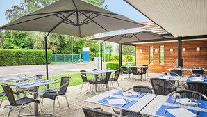 Un patio al aire libre con mesas y sillas, sombrillas y vistas a una carretera y vegetación.