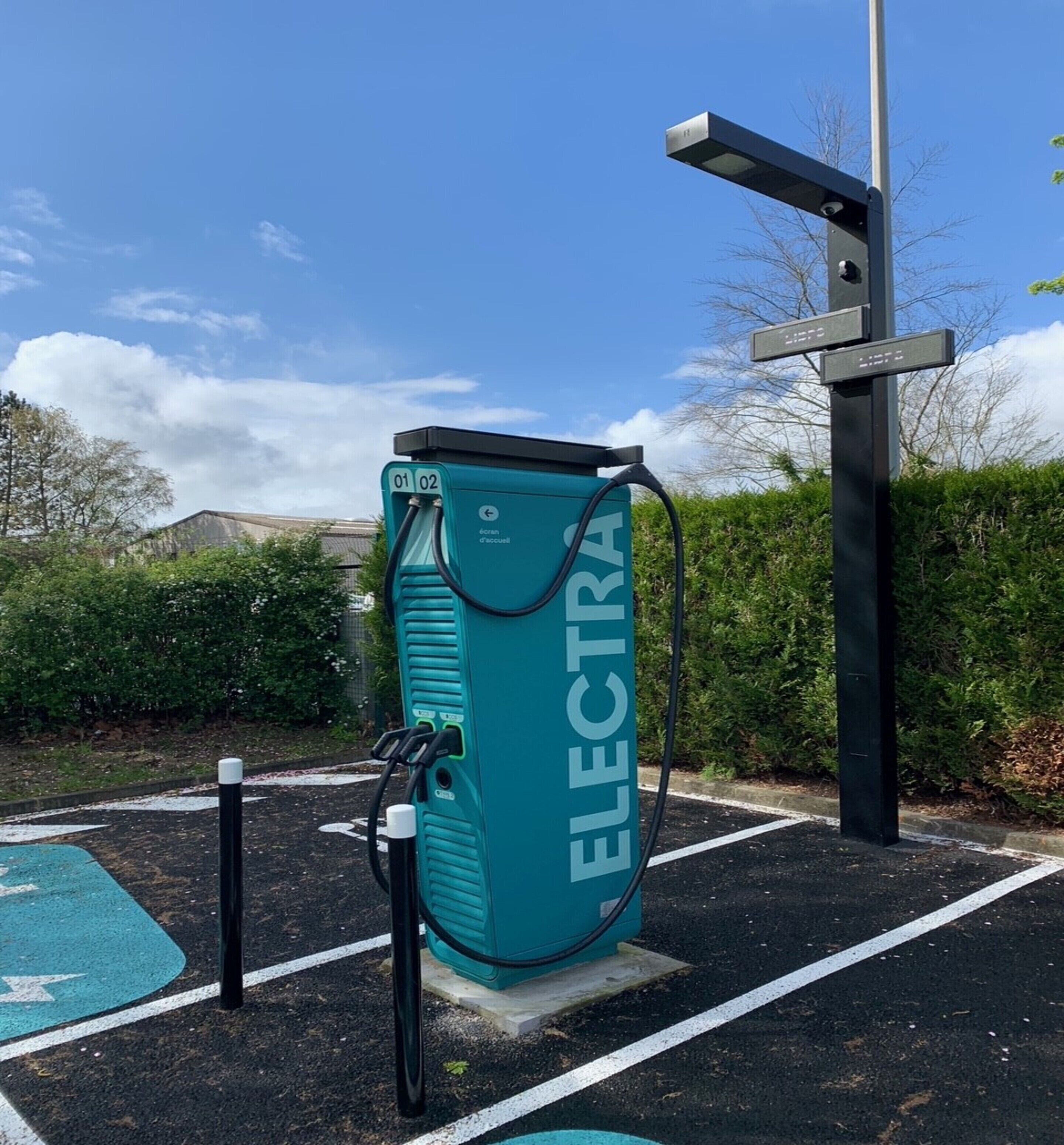 A teal electric vehicle charging station with a sign indicating it is a public charging point.