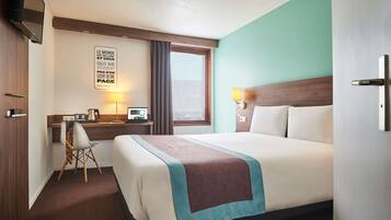Habitación de hotel con una cama grande, un escritorio con computadora, una silla y un ventanal con cortinas.