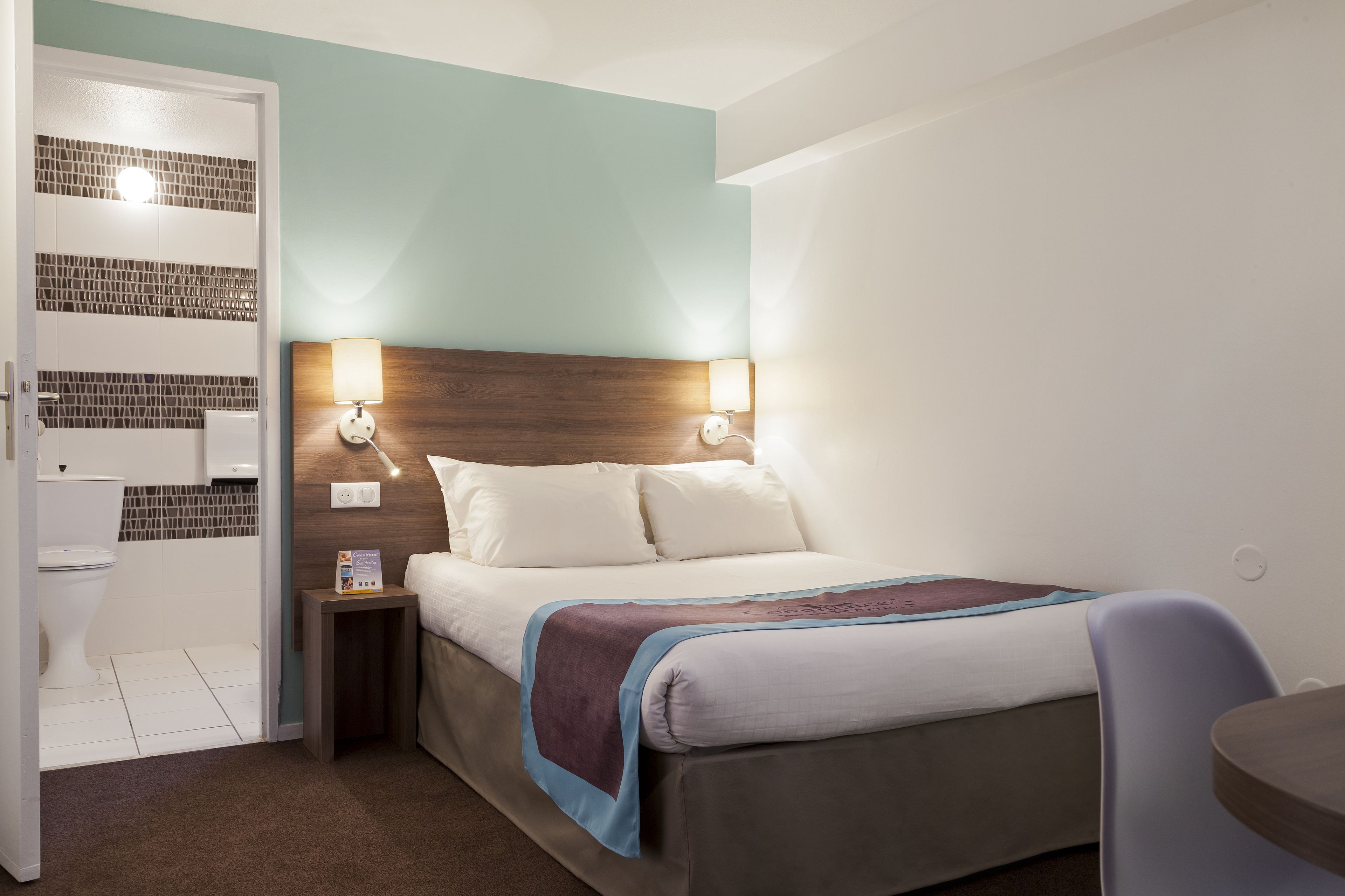 Habitació d'hotel amb llit, làmpades de nit, una taula de nit, una cadira i una taula petita.