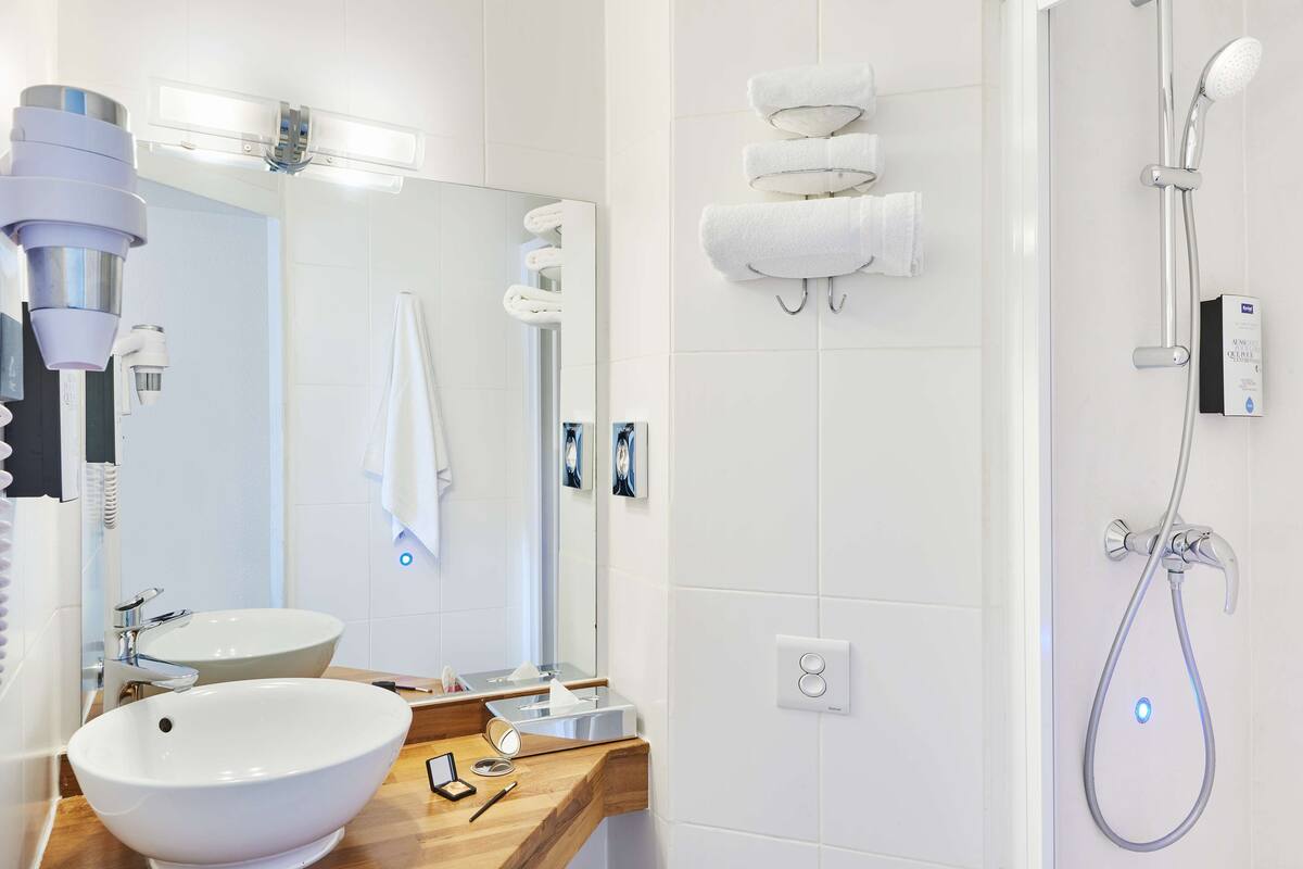 A modern bathroom with a large mirror, two sinks, a shower, and a towel rack.